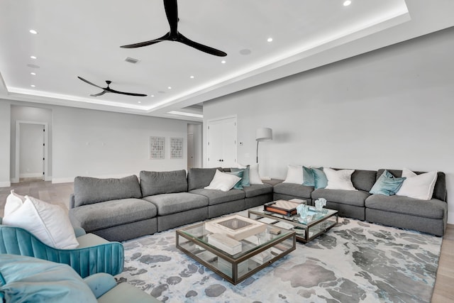 living room featuring light wood-type flooring, ceiling fan, and a tray ceiling