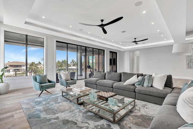 living room with ceiling fan, a raised ceiling, and light wood-type flooring