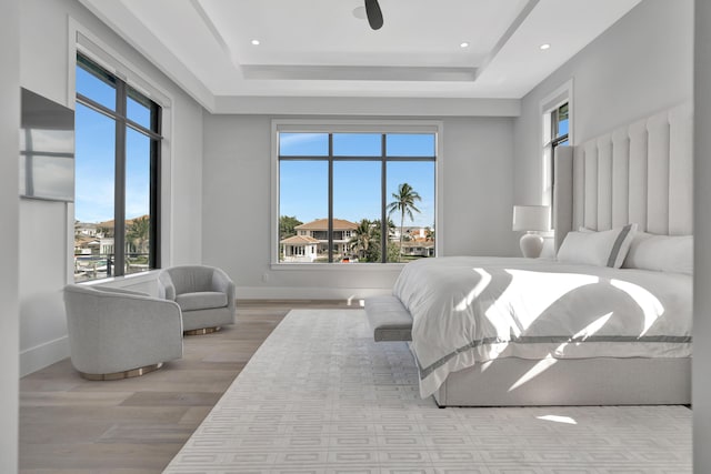 bedroom featuring ceiling fan, a raised ceiling, and light wood-type flooring