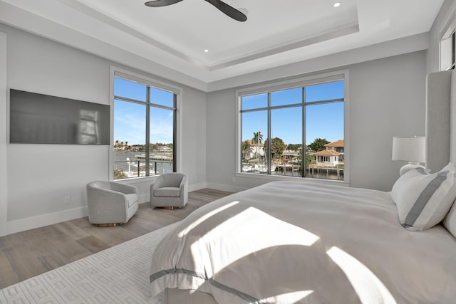 bedroom featuring a water view, ceiling fan, light hardwood / wood-style floors, and a tray ceiling