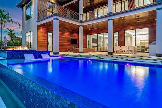 pool at dusk with ceiling fan, a fire pit, and a patio