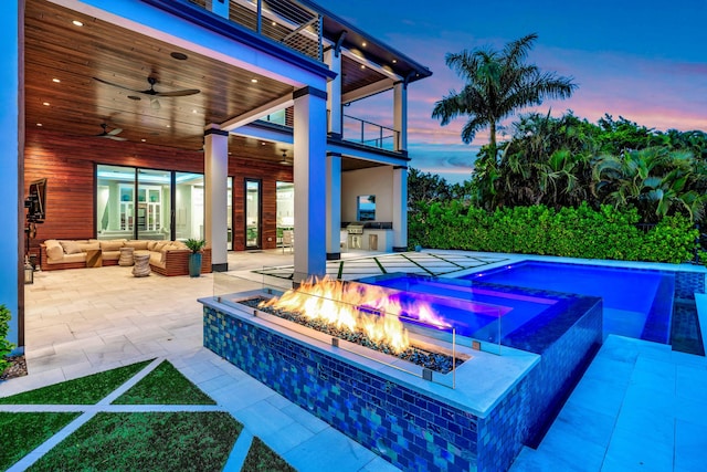 pool at dusk with ceiling fan, an outdoor living space with a fire pit, a patio area, and area for grilling