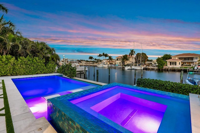 pool at dusk with a water view, a dock, and an in ground hot tub