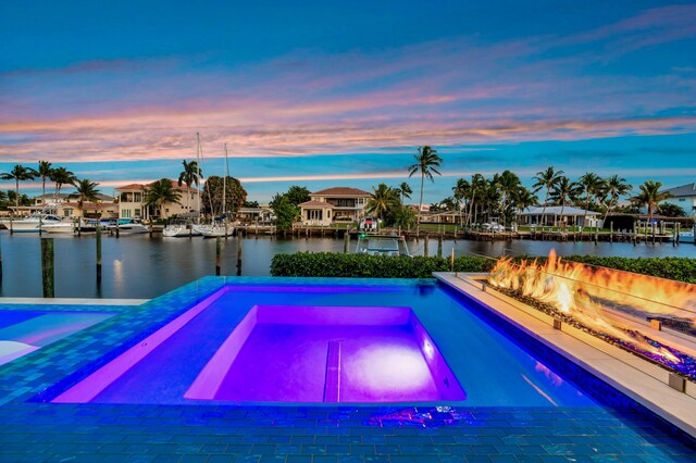 pool at dusk featuring a water view and an in ground hot tub