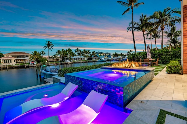 pool at dusk featuring a water view, a boat dock, a patio, and an in ground hot tub