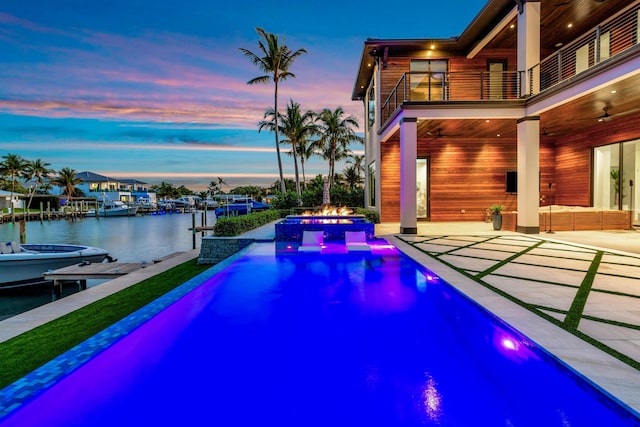 pool at dusk featuring ceiling fan, outdoor lounge area, a hot tub, a water view, and a patio