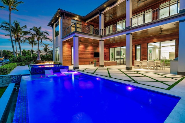 pool at dusk featuring ceiling fan, a patio area, and an in ground hot tub