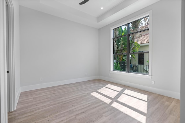 empty room featuring ceiling fan, a tray ceiling, and light hardwood / wood-style flooring