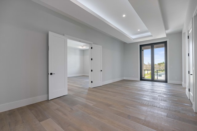 spare room featuring a tray ceiling, light hardwood / wood-style flooring, and french doors