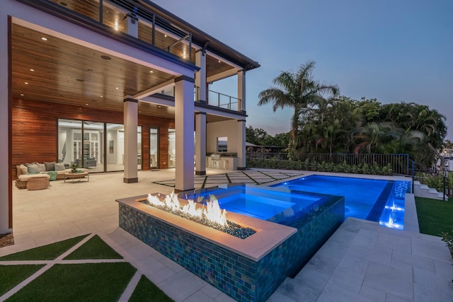 pool at dusk with an outdoor living space with a fire pit, an outdoor kitchen, an in ground hot tub, and a patio