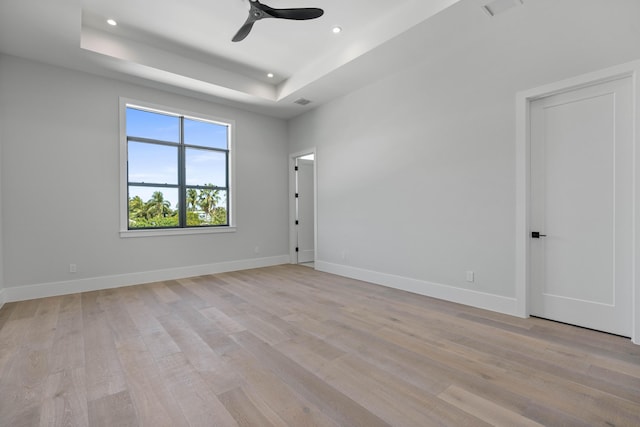 unfurnished room featuring ceiling fan, a tray ceiling, and light hardwood / wood-style floors