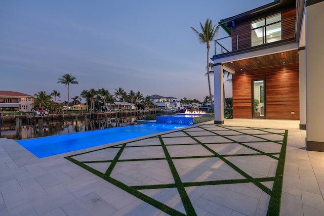 pool at dusk with a water view, pool water feature, and a patio