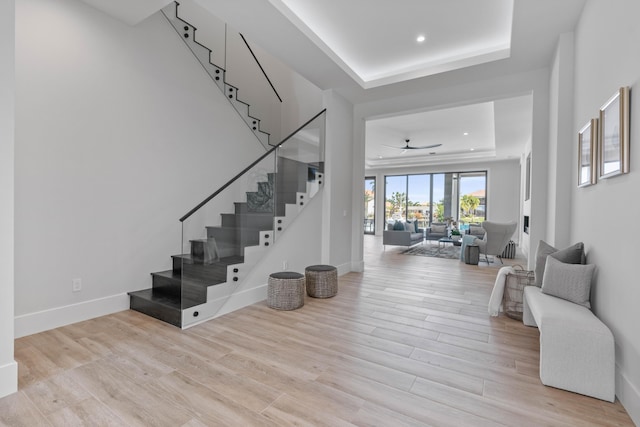 stairs featuring ceiling fan, wood-type flooring, and a tray ceiling