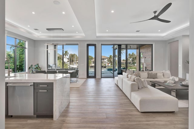 living room featuring ceiling fan, a healthy amount of sunlight, light hardwood / wood-style flooring, and a raised ceiling