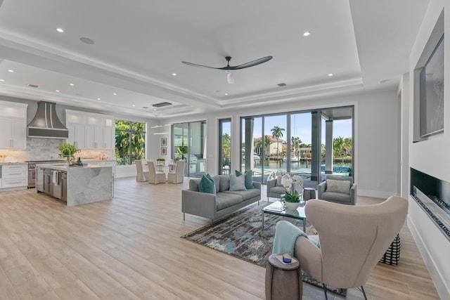 living room with ceiling fan, light hardwood / wood-style floors, a wealth of natural light, and a raised ceiling