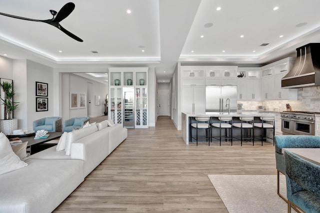 living room with ceiling fan, a tray ceiling, and light wood-type flooring