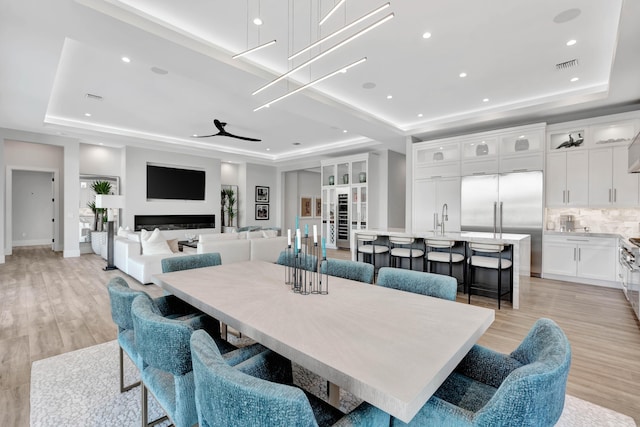 dining room with ceiling fan, sink, a tray ceiling, and light hardwood / wood-style floors