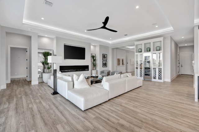 living room with ceiling fan, a tray ceiling, and light hardwood / wood-style flooring