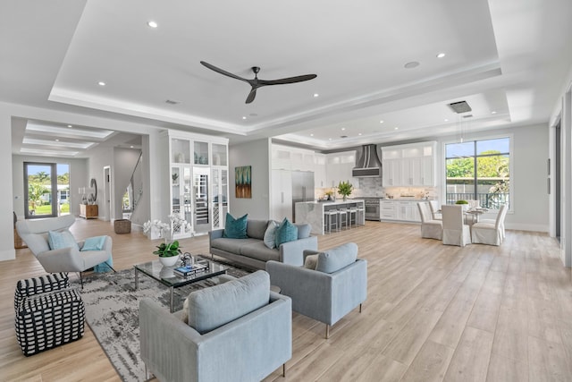 living room featuring a raised ceiling, a healthy amount of sunlight, ceiling fan, and light hardwood / wood-style floors