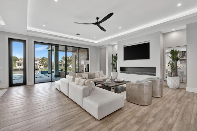 living room with ceiling fan, light hardwood / wood-style floors, and a tray ceiling