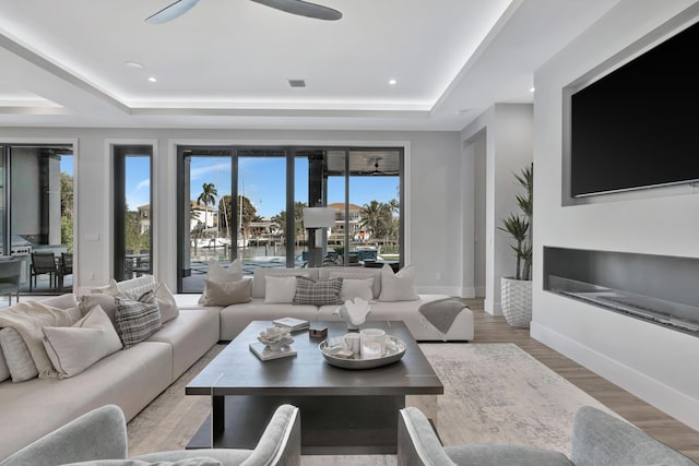 living room featuring light hardwood / wood-style floors, a raised ceiling, and ceiling fan