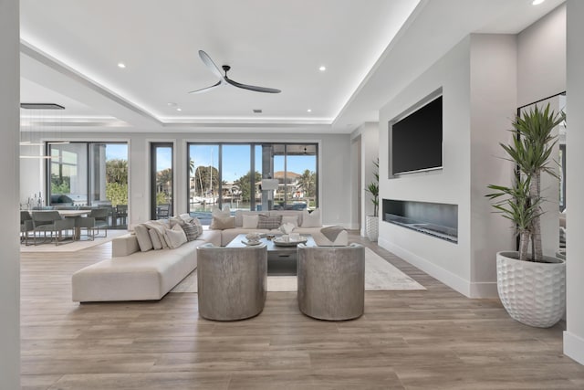 living room featuring ceiling fan, a raised ceiling, and plenty of natural light