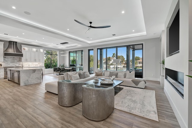 living room featuring ceiling fan, a raised ceiling, and light wood-type flooring