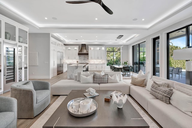 living room featuring light wood-type flooring, ceiling fan, and a tray ceiling