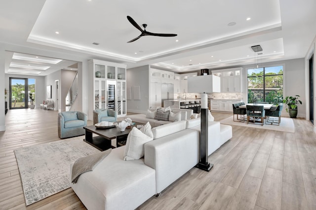 living room featuring french doors, sink, a raised ceiling, ceiling fan, and light hardwood / wood-style flooring