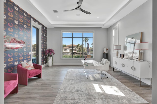 sitting room with ceiling fan, light hardwood / wood-style floors, and a tray ceiling