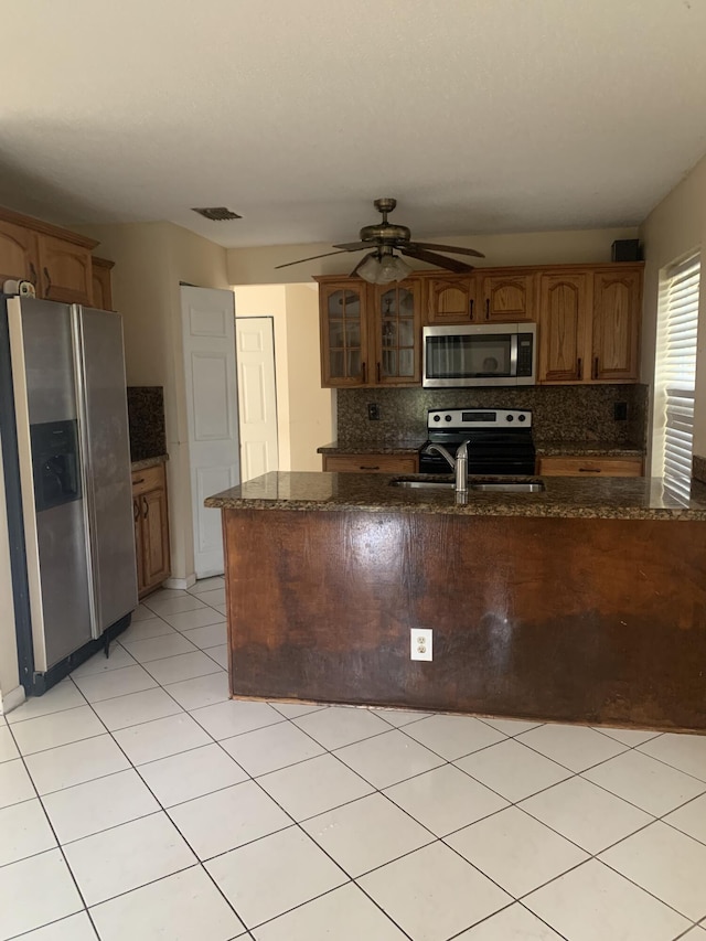 kitchen featuring sink, dark stone countertops, appliances with stainless steel finishes, ceiling fan, and decorative backsplash