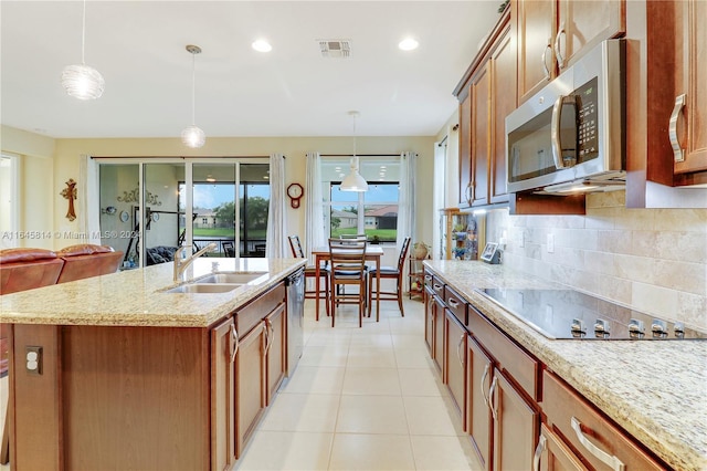 kitchen with a center island with sink, sink, decorative backsplash, appliances with stainless steel finishes, and decorative light fixtures