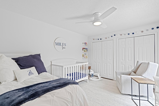 bedroom featuring ceiling fan, light colored carpet, a textured ceiling, and two closets