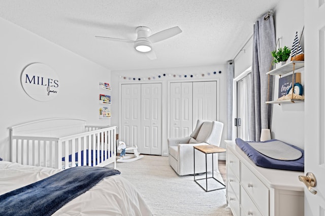 carpeted bedroom with multiple closets, a textured ceiling, and ceiling fan