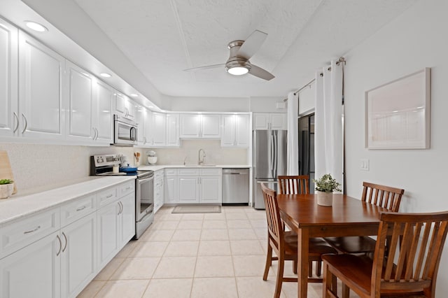 kitchen with light tile patterned floors, ceiling fan, appliances with stainless steel finishes, white cabinets, and decorative backsplash