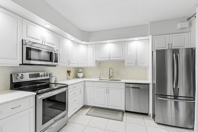 kitchen featuring sink, stainless steel appliances, tasteful backsplash, white cabinets, and light tile patterned flooring