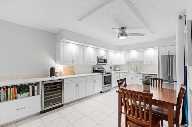 kitchen with light tile patterned flooring, sink, white cabinetry, appliances with stainless steel finishes, and beverage cooler