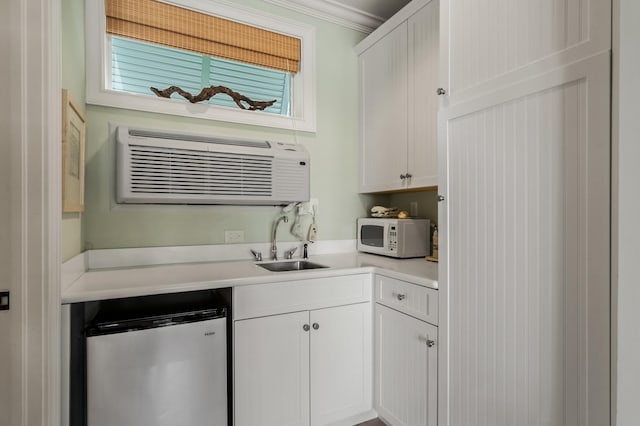 kitchen featuring an AC wall unit, crown molding, sink, fridge, and white cabinetry