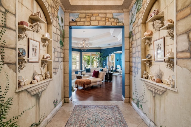 hallway with light tile patterned floors, a tray ceiling, crown molding, and a notable chandelier