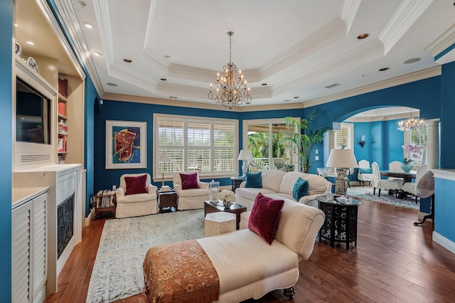 living room featuring dark hardwood / wood-style floors, a raised ceiling, ornamental molding, and an inviting chandelier