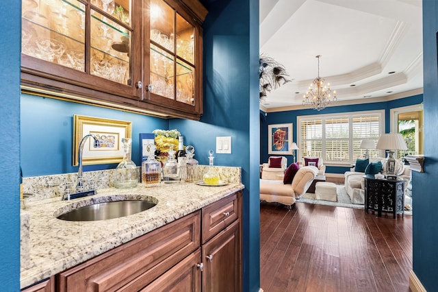 bar with light stone countertops, a raised ceiling, crown molding, sink, and decorative light fixtures