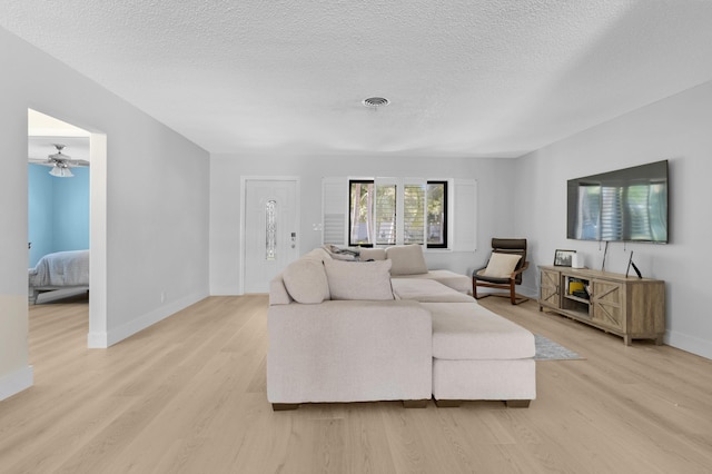 living area featuring light wood finished floors, visible vents, baseboards, and a textured ceiling