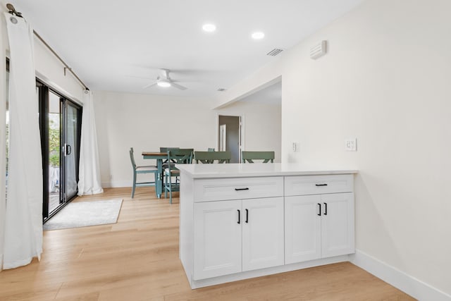 kitchen with light wood-style flooring, a peninsula, visible vents, baseboards, and white cabinetry