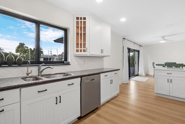 kitchen with backsplash, stainless steel dishwasher, white cabinets, a sink, and light wood-type flooring