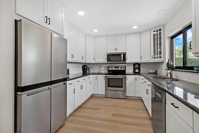 kitchen with light wood-style flooring, a sink, white cabinets, appliances with stainless steel finishes, and backsplash