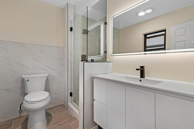 bathroom featuring toilet, a shower with door, vanity, and tile walls