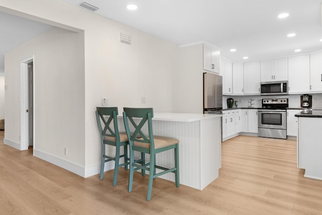 kitchen with visible vents, white cabinetry, appliances with stainless steel finishes, light wood-type flooring, and decorative backsplash