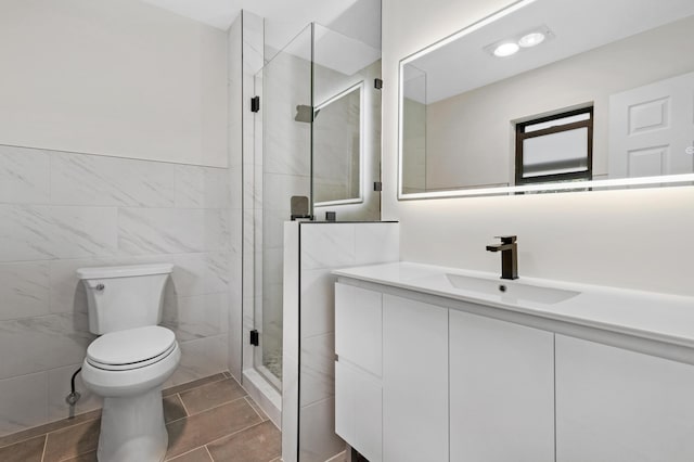 full bath with a stall shower, toilet, tile patterned flooring, vanity, and tile walls