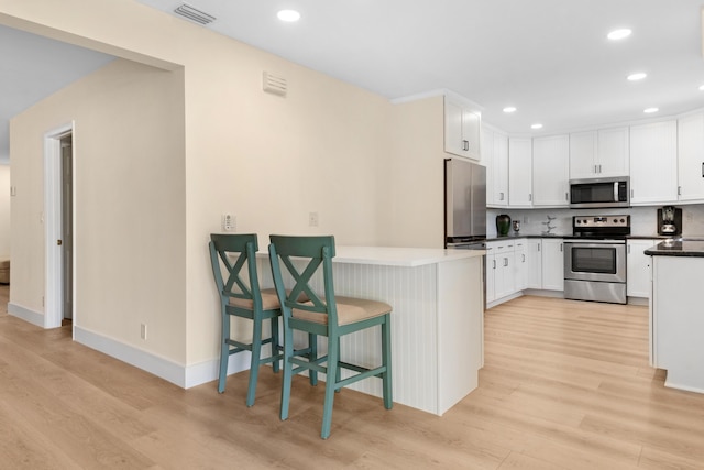 kitchen with a breakfast bar area, appliances with stainless steel finishes, decorative backsplash, light wood-type flooring, and white cabinets