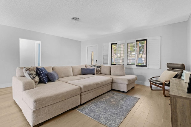 living area with baseboards, light wood-style flooring, visible vents, and a textured ceiling